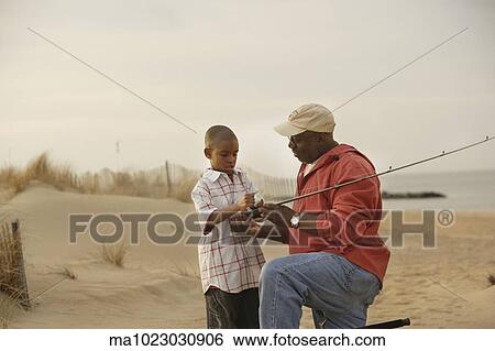 Stock Photograph - African father and son on beach with fishing gear. Fotosearch