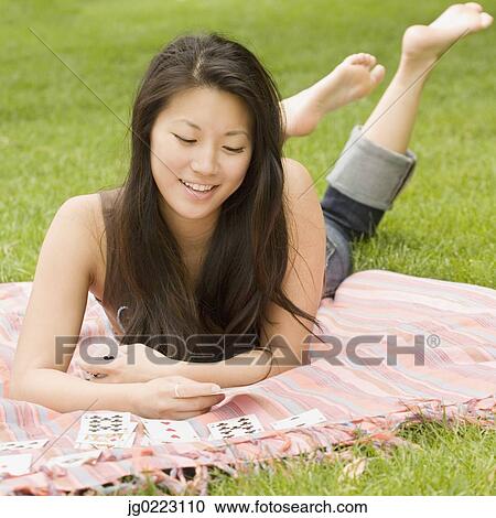 Stock Image - Asian woman playing solitaire on blanket in grass. Fotosearch