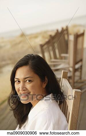 Stock Photograph - Asian woman sitting on deck at beach. Fotosearch