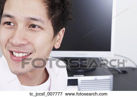 Stock Photo - Close up of young Asian man next to computer. Fotosearch