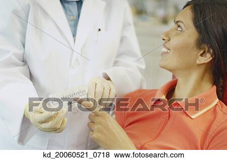 Dental patient choosing tooth color sample from dentist View Large Photo Image Stock Photo - Dental patient choosing tooth color sample from dentist. Fotosearch
