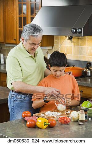 Picture - Hispanic father and son chopping vegetables in kitchen. Fotosearch
