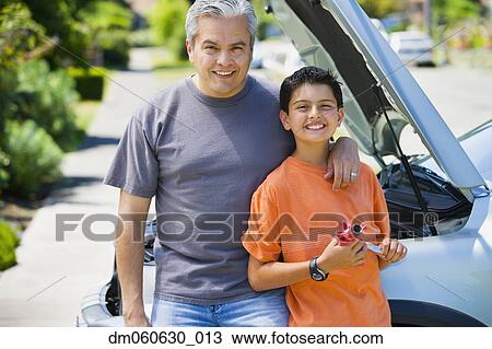 Stock Image - Hispanic father and son standing in front of car with hood up. Fotosearch