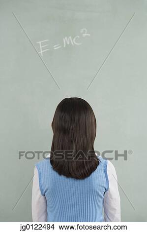Picture - Hispanic girl looking at formula written on blackboard. Fotosearch