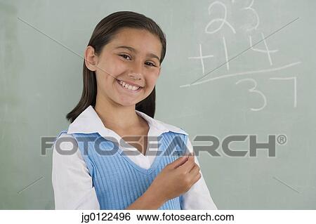 Stock Photograph - Hispanic girl smiling in front of blackboard. Fotosearch