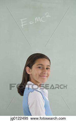 Stock Photography - Hispanic girl smiling in front of blackboard. Fotosearch