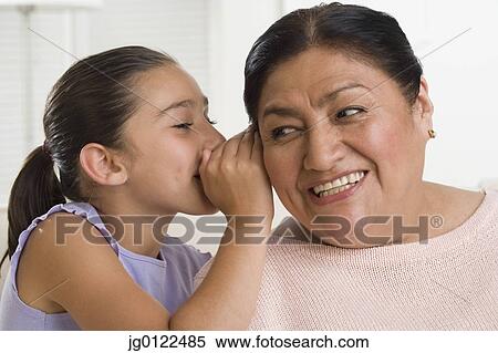 Stock Photography - Hispanic girl whispering in grandmother's ear. Fotosearch