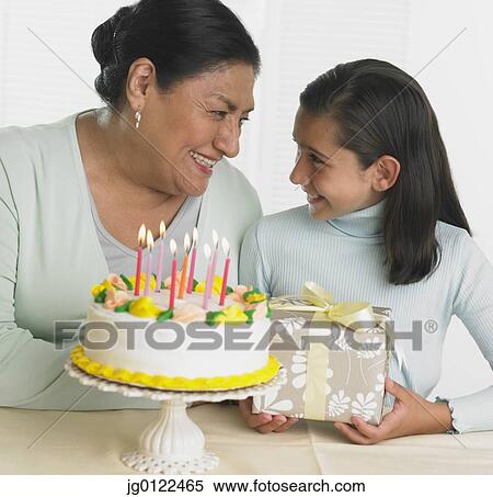 Stock Photography - Hispanic grandmother and granddaughter with birthday cake and gift. Fotosearch