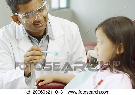 Indian male dentist with Asian girl in dentist's chair View Large Photo Image Stock Image - Indian male dentist with Asian girl in dentist's chair. Fotosearch