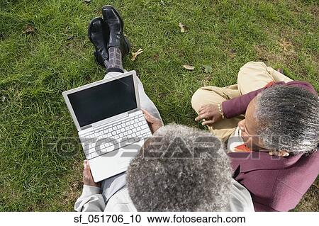 Stock Image - Senior African couple using laptop on grass outdoors. Fotosearch