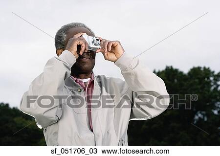Stock Image - Senior African man talking photograph outdoors. Fotosearch
