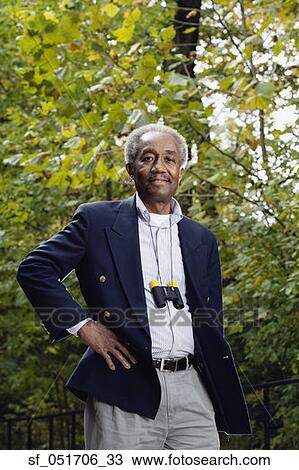 Stock Image - Senior African man with binoculars around neck in woods. Fotosearch