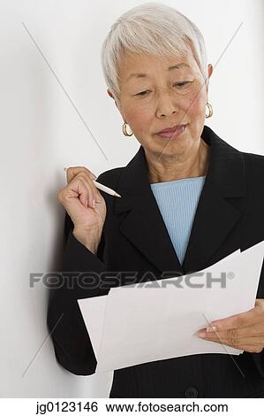 Stock Photograph - Senior Asian businesswoman reading paperwork. Fotosearch