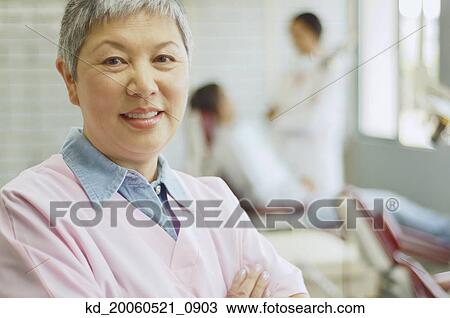 Senior Asian female dental assistant with dentist and patient in background View Large Photo Image Stock Image - Senior Asian female dental assistant with dentist and patient in background. Fotosearch