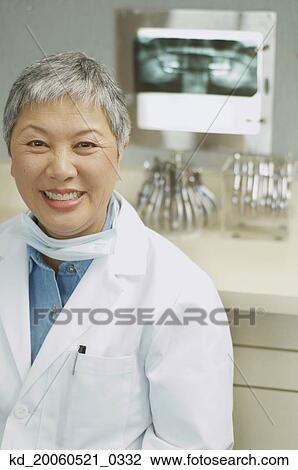 Stock Image - Senior Asian female dentist smiling next to x-rays. Fotosearch