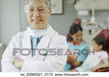 Senior Asian female dentist with assistant and patient in background View Large Photo Image Stock Image - Senior Asian female dentist with assistant and patient in background. Fotosearch