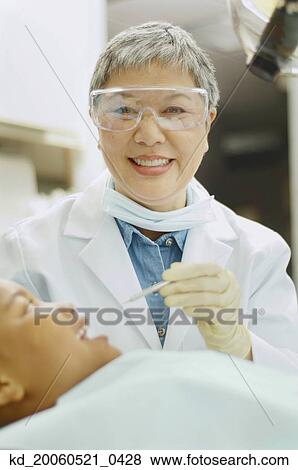 Stock Photo - Senior Asian female dentist working on African boy. Fotosearch