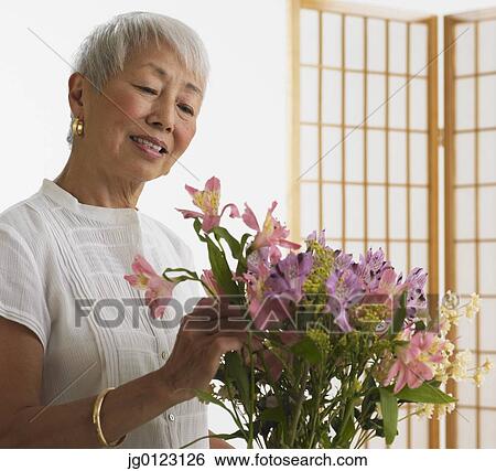Stock Photograph - Senior Asian woman arranging flowers indoors. Fotosearch