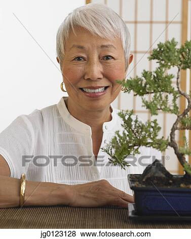 Senior Asian woman smiling with bonsai tree indoors View Large Photo Image Stock Photo - Senior Asian woman smiling with bonsai tree indoors. Fotosearch
