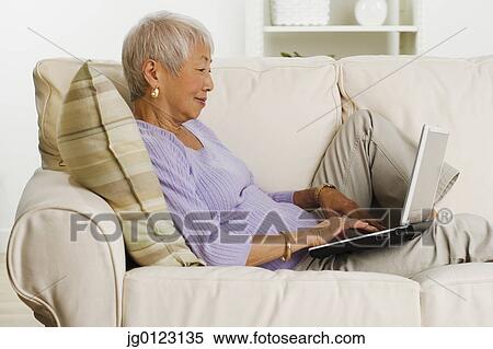 Senior Asian woman using laptop on sofa View Large Photo Image Stock Photography - Senior Asian woman using laptop on sofa. Fotosearch