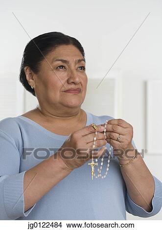 Picture - Senior Hispanic woman praying with rosary. Fotosearch