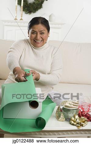 Stock Photo - Senior Hispanic woman wrapping gift in livingroom. Fotosearch
