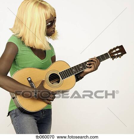 Stock Image - Studio shot of African woman wearing blonde wig and playing guitar. Fotosearch