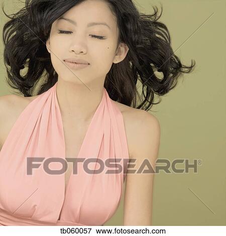 Stock Photo - Studio shot of Asian woman with hair blowing and eyes closed. Fotosearch