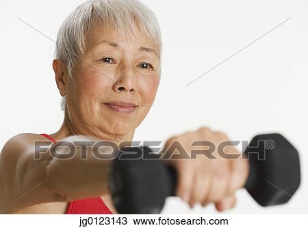 Stock Image - Studio shot of senior Asian woman holding dumbbell. Fotosearch