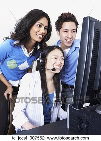 Stock Image - Young Asian female computer service technician with coworkers looking over her shoulder . Fotosearch