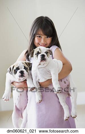 Stock Image - Young Asian girl smiling and holding two puppies. Fotosearch
