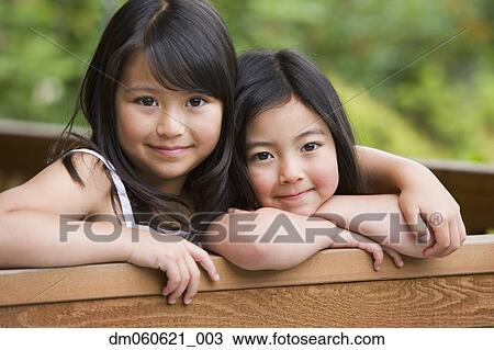 Stock Image - Young Asian sisters hugging and smiling outdoors. Fotosearch