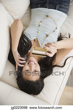 Young Asian woman using telephone and credit card on sofa View Large Photo Image Stock Photo - Young Asian woman using telephone and credit card on sofa. Fotosearch