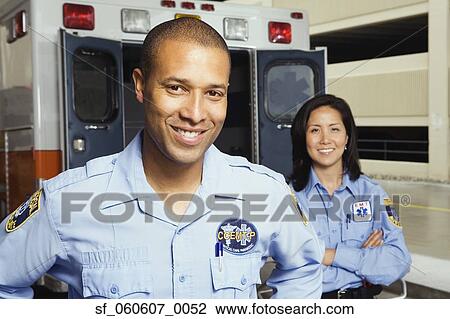 Stock Image - African male and Asian female paramedics smiling in front of ambulance. Fotosearch