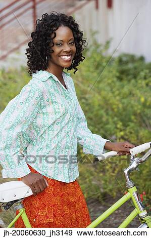 Stock Photo - African woman smiling and walking bicycle. Fotosearch
