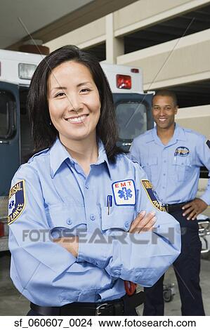 Picture - Asian female paramedic smiling in front of ambulance. Fotosearch