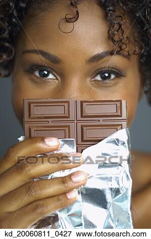 Stock Photo - Close up of African woman holding chocolate in front of face. Fotosearch