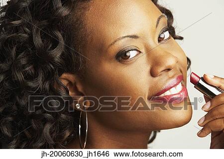 Stock Photograph - Close up of African woman holding lipstick next to lips. Fotosearch