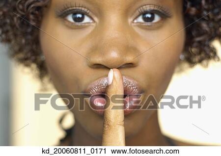 Stock Image - Close up of African woman with finger up to lips. Fotosearch