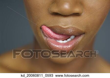 Stock Image - Close up of African woman's mouth with tongue licking lips. Fotosearch
