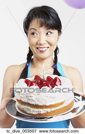 Stock Photo - Close up of Asian woman holding cake with candle. Fotosearch