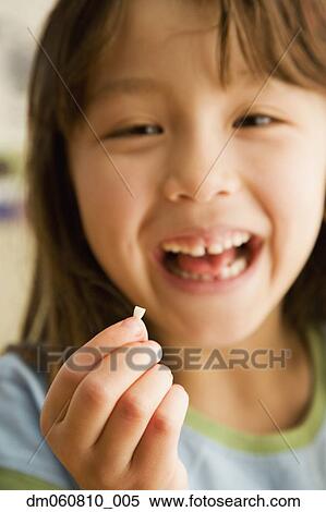 Stock Photography - Close up of young girl smiling and holding tooth. Fotosearch