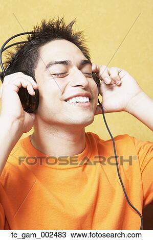 Stock Image - Close up of young man listening to headphones indoors. Fotosearch