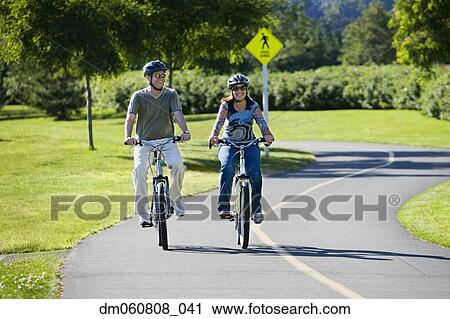 Couple riding bicycles in park View Large Photo Image Stock Image - Couple riding bicycles in park. Fotosearch