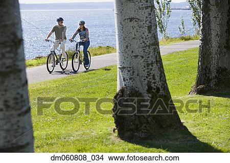 Picture - Couple riding bicycles next to water. Fotosearch