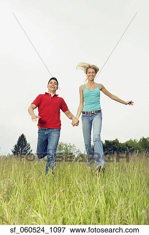 Stock Photo - Couple running and holding hands in meadow. Fotosearch