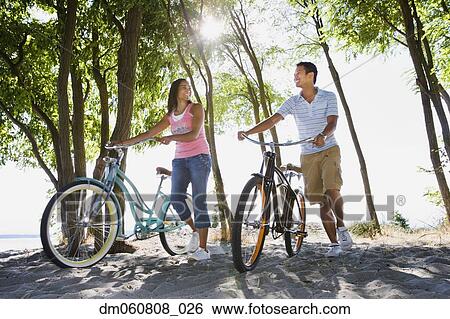 Stock Photograph - Couple walking with bicycles on beach. Fotosearch