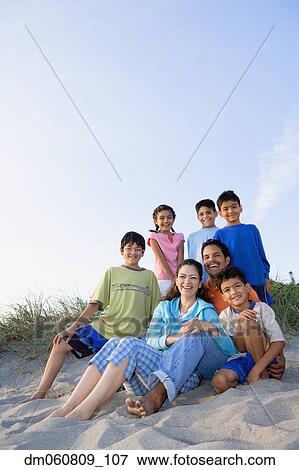Stock Photo - Hispanic family sitting on beach smiling. Fotosearch