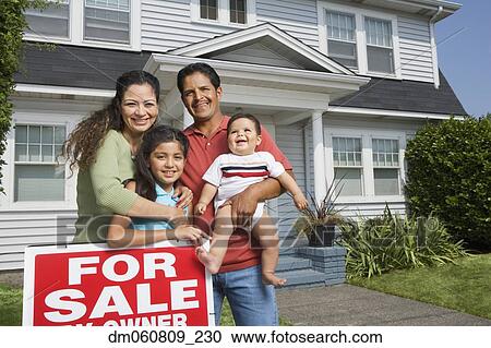 Stock Image - Hispanic family standing next to For Sale sign in front of house. Fotosearch