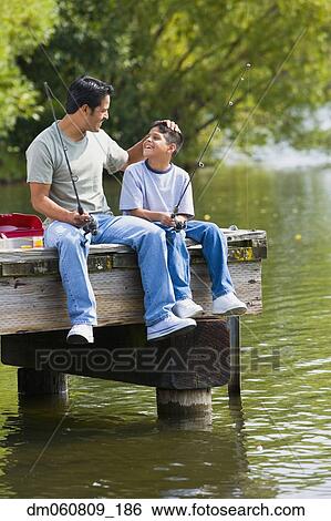 Stock Photograph - Hispanic father and son sitting on dock with fishing poles. Fotosearch